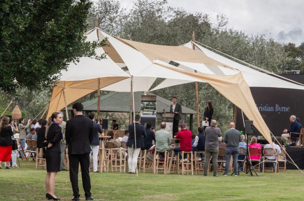 An outdoor investment presentation event in Sotogrande, with attendees seated under a stylish canopy listening to speakers on stage.