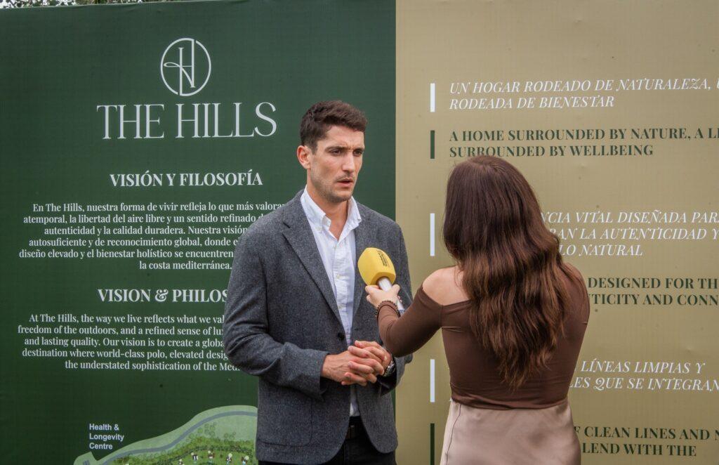 A man in a blazer is interviewed in front of The Hills display board at a Sotogrande investment event, discussing the project’s vision and philosophy.