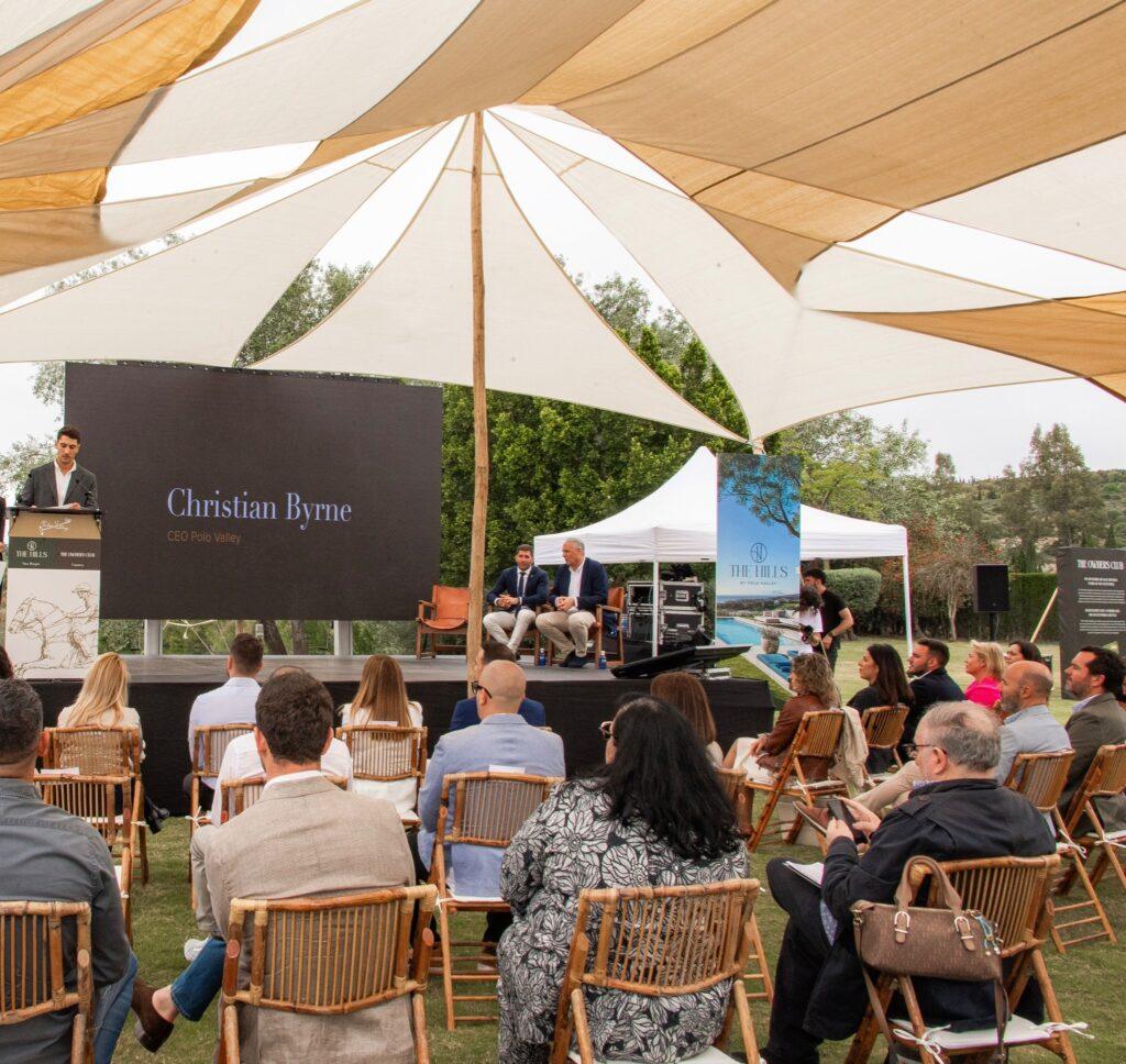 Christian Byrne presents at an outdoor Sotogrande investment event, addressing seated attendees under a canopy beside promotional displays.