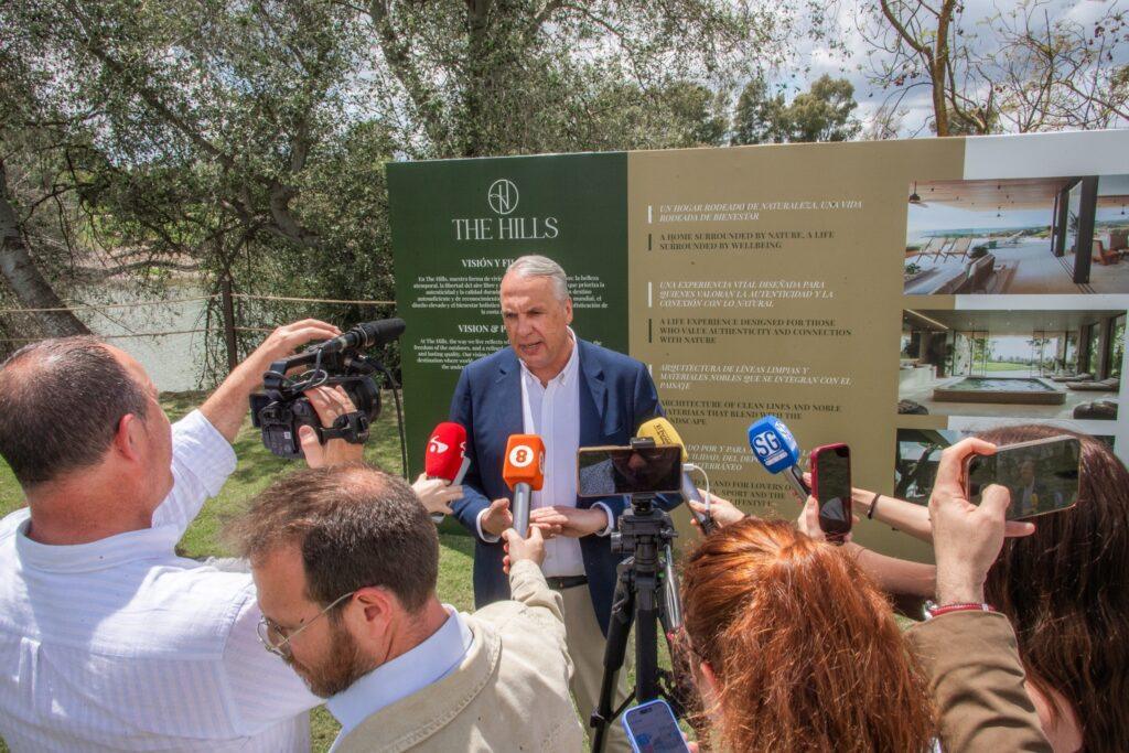 A man speaks to reporters and TV crews in front of a promotional display for The Hills during a Sotogrande investment event.