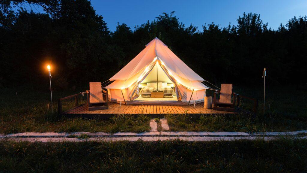 Luxury glamping tent illuminated at night with cozy interior and outdoor seating on a wooden deck